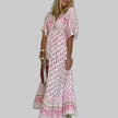 Woman wearing a pink boho maxi dress with all-over floral block print and V-neckline, gray background