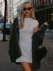 Woman wearing a white cap sleeve mini dress with a dark fuzzy cardigan