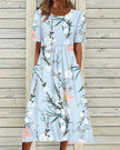 Woman wearing a light blue floral midi dress with side pockets, front view against wooden fence