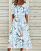 Woman wearing a light blue floral midi dress with side pockets, front view against wooden fence