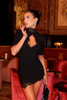 Woman wearing a black lace bodycon mini dress with a high neckline in a lounge setting