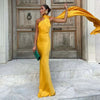 Woman wearing a yellow one-shoulder evening gown with a flowing sash in the wind