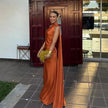 Woman wearing an orange one-shoulder evening gown with a draped shoulder sash