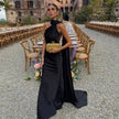 Woman wearing a black one-shoulder draped evening gown with a long trailing sash