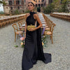 Woman wearing a black one-shoulder draped evening gown with a long trailing sash