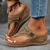 Brown wedge sandal with laser-cut strap worn on a foot next to jeans