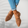 Woman crossing ankles wearing brown suede pointed-toe loafers