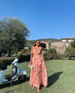 Woman standing outdoors wearing an orange floral ruffle maxi dress with a waist cutout