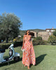 Woman standing outdoors wearing an orange floral ruffle maxi dress with a waist cutout