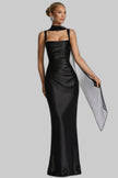 Woman wearing a black satin evening gown with a draped sheer scarf over one shoulder