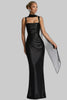 Woman wearing a black satin evening gown with a draped sheer scarf over one shoulder