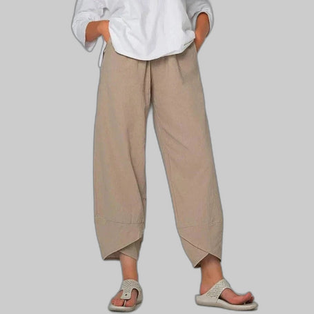 Woman wearing khaki wide leg casual pants with asymmetric cropped hem and drawstring waist, styled with white top and sandals, gray background